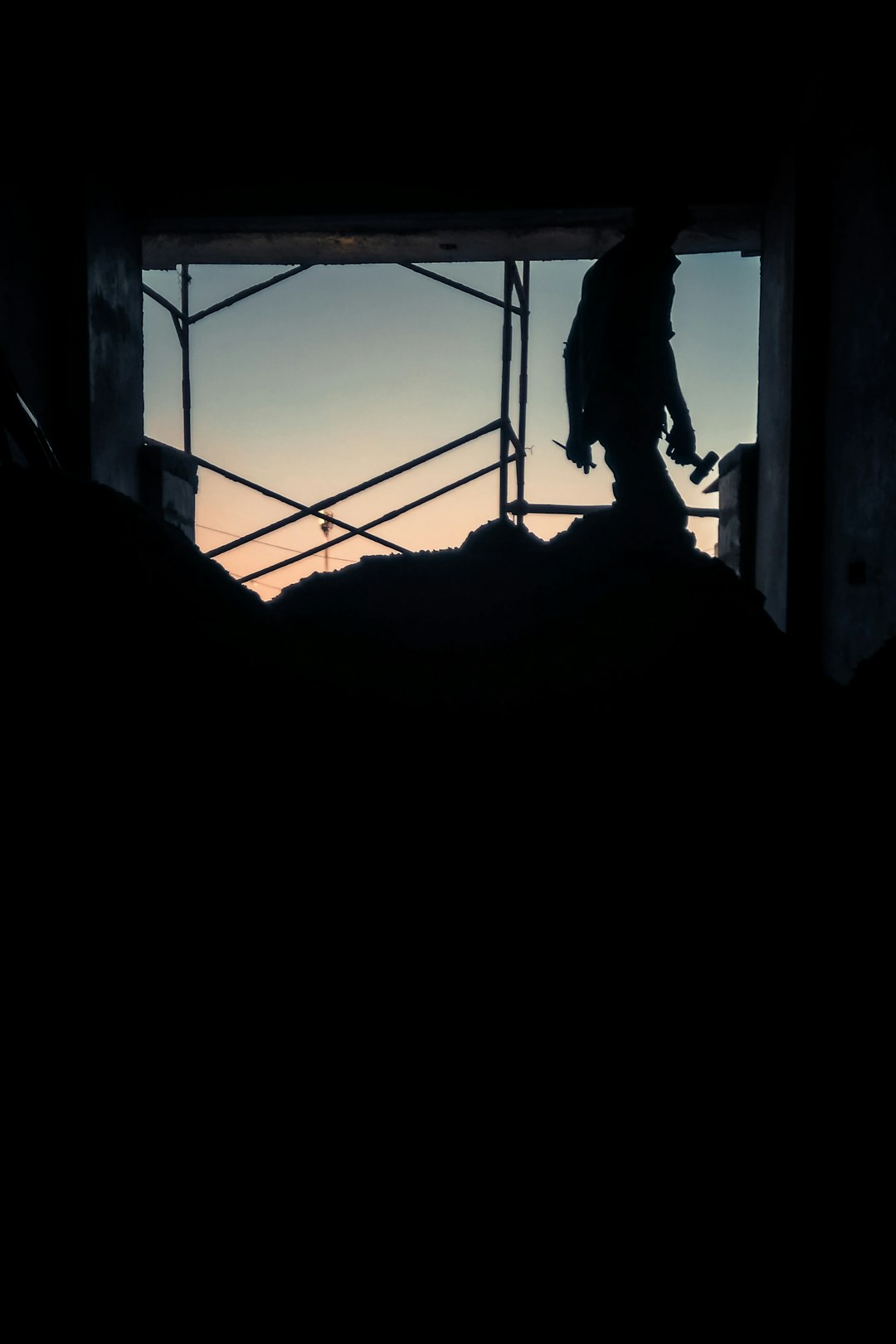 Silhouetted factory worker standing on vast industrial floor at dusk