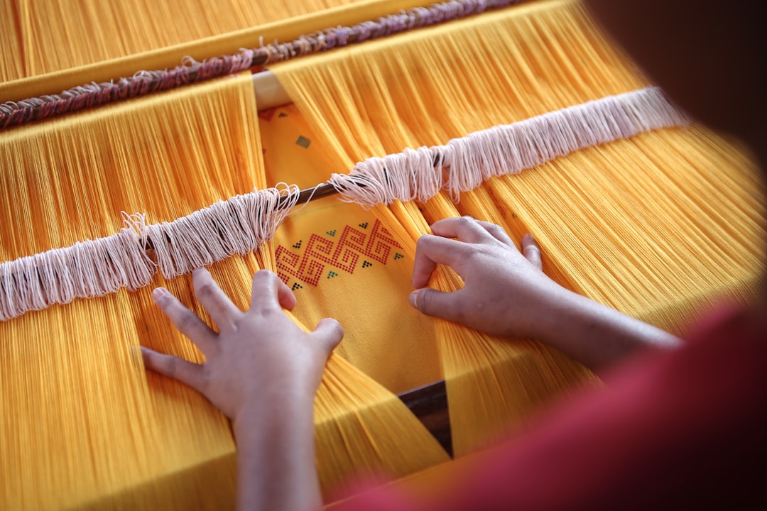 Weaver's hands guiding gold threads on traditional loom