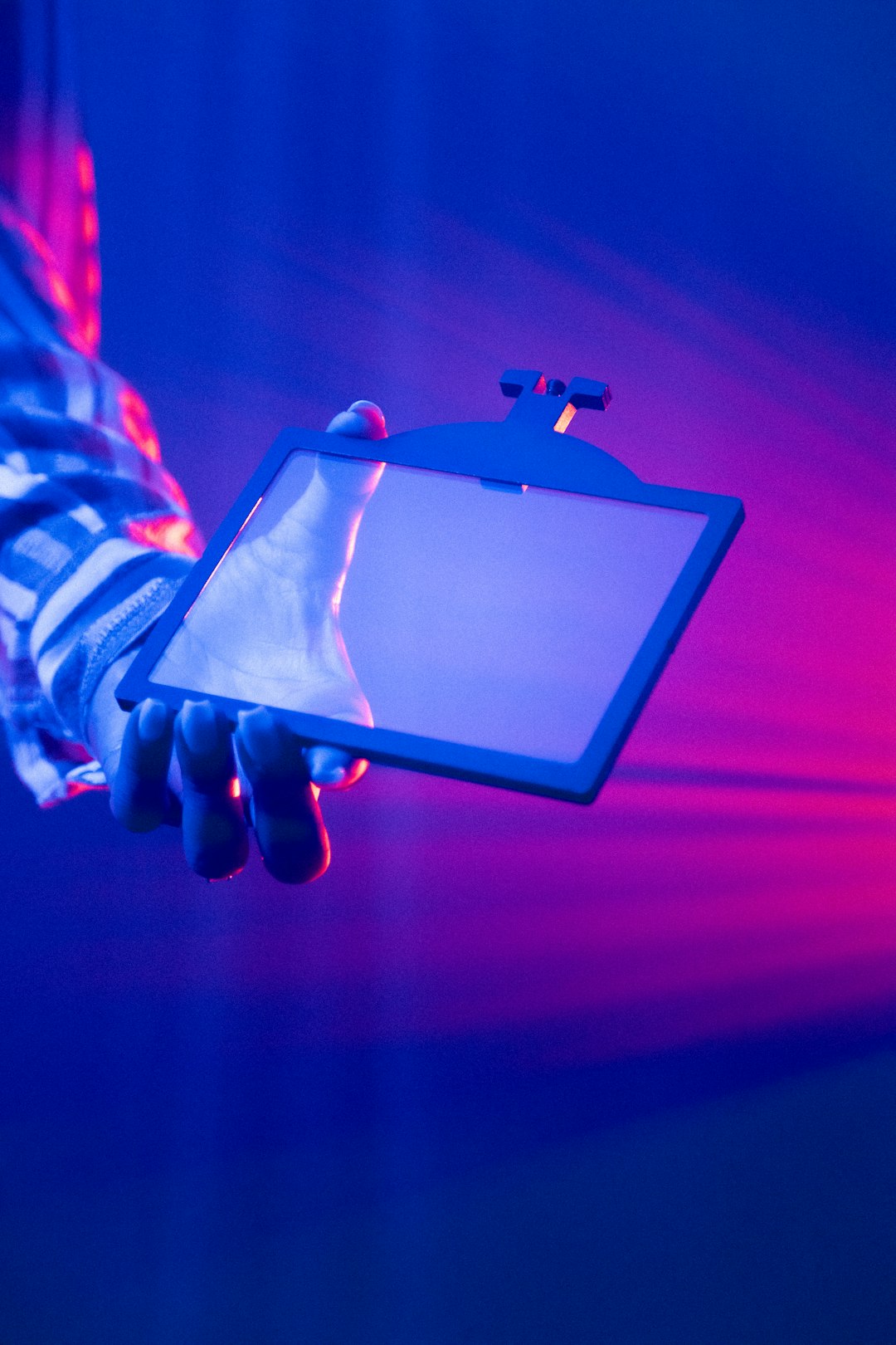 Hand holding tablet with laptop in background