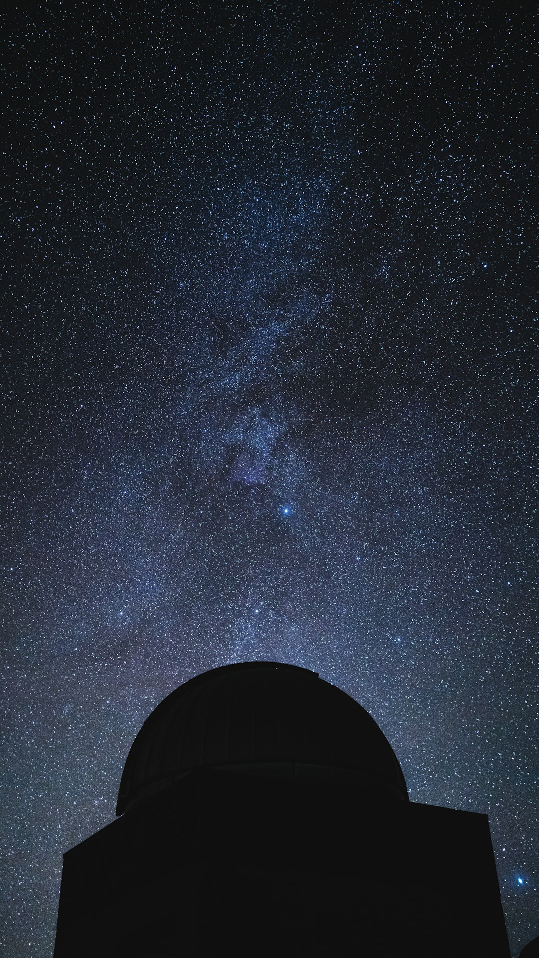 Silhouetted astronomer beneath open observatory dome with star trails