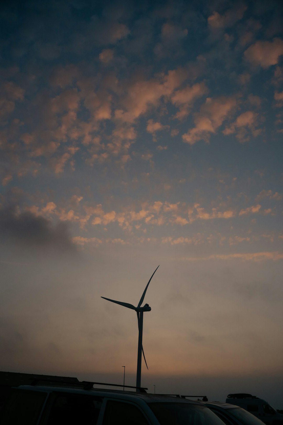 Electric car silhouette against sunset with wind turbines
