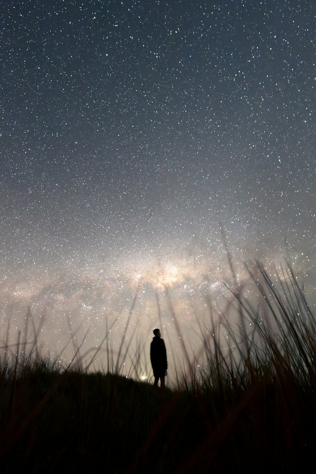 Person gazing at star-filled night sky from dark hillside